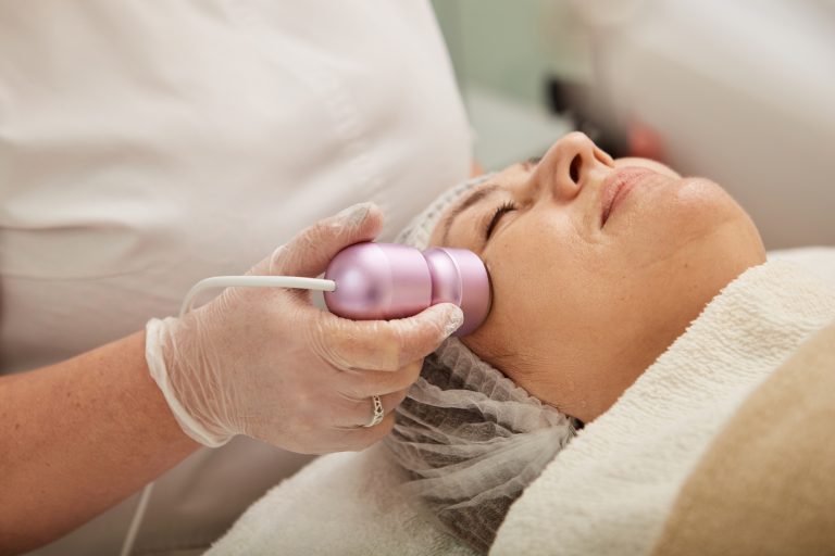 Cosmetologist massaging woman face with cryotherapy massager